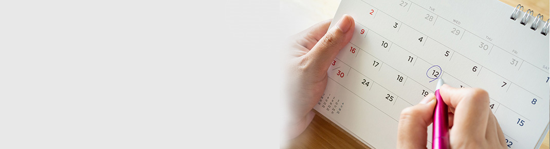 Kvinne i briller iført en mørkeblå skjorte lener seg på en hvit seng med et smil og ser ettertenksom ut. / Nærbilde av en kalender med en kvinnes hånd som markerer en dag med penn.
